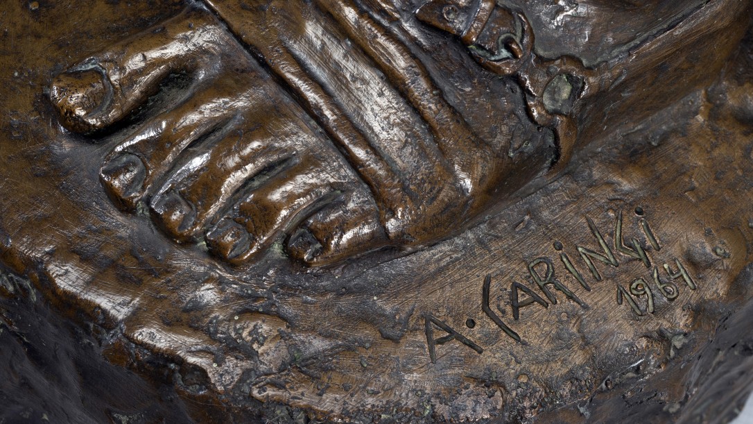 Escultura em bronze representando o "gaúcho laçador". Figura masculina, em pé, apoiada sobre a perna esquerda, corpo e cabeça virada para frente. A cabeça, com cabelos na altura do pescoço, possui uma faixa amarrada na testa, barba e bigode.